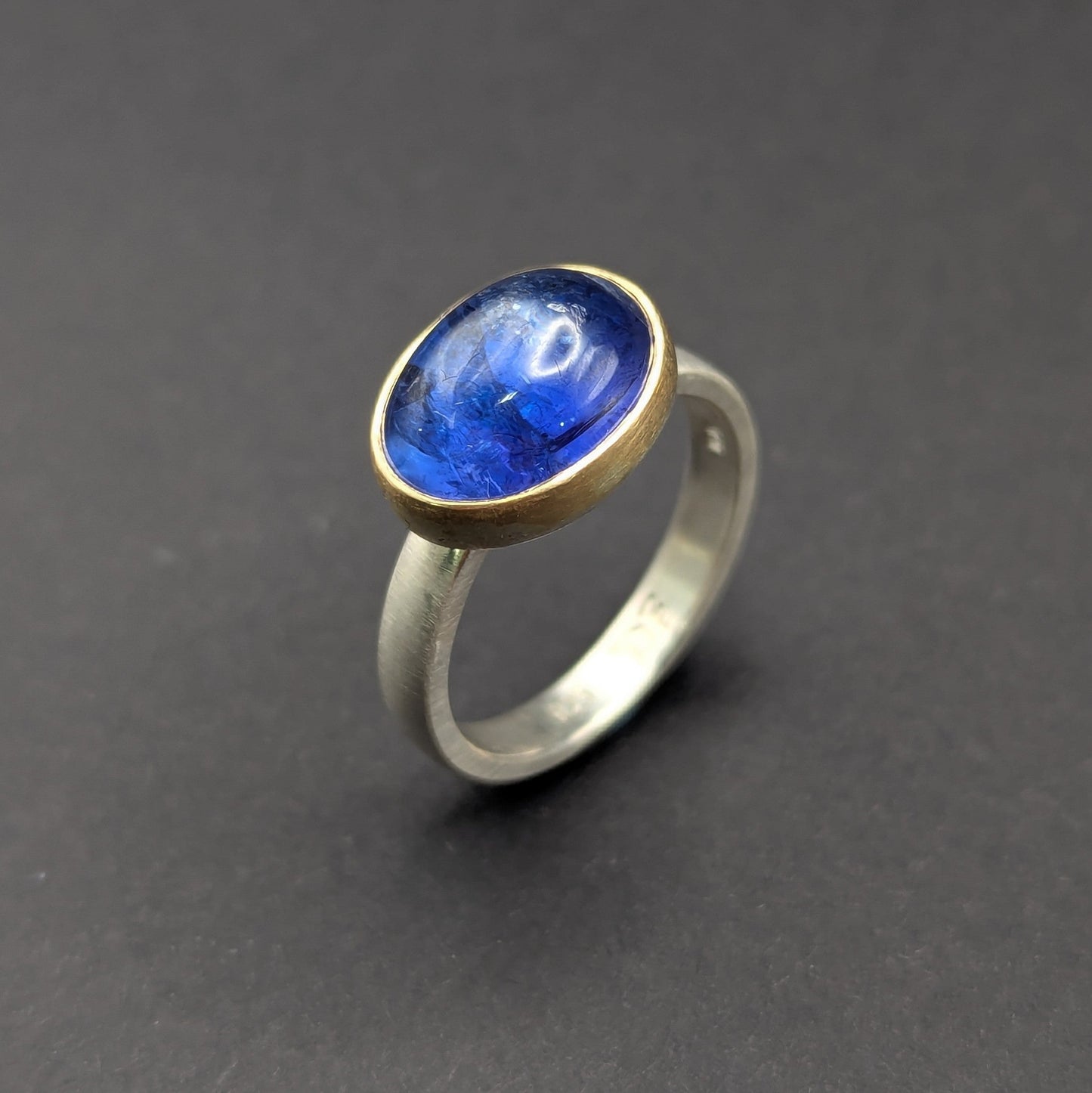 Ring with a blue gemstone and gold accent on a dark gray background
