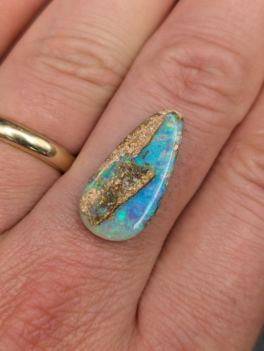 A close-up of a teardrop-shaped opal gemstone with vibrant blue and green flashes and a textured gold pattern.